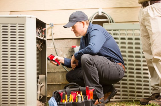 Mid-adult repairman works on a home's Orem, UT air conditioner unit outdoors. Man center is working on the unit using tools in his toolbox.
